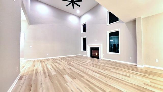 unfurnished living room with a high ceiling, light hardwood / wood-style flooring, and ceiling fan