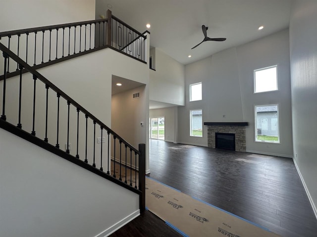 unfurnished living room featuring ceiling fan, stairs, wood finished floors, a towering ceiling, and visible vents
