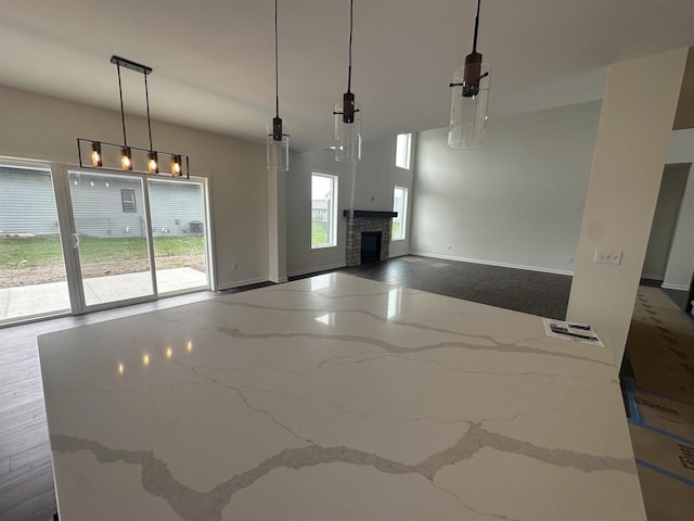 kitchen featuring baseboards, hanging light fixtures, a fireplace, and light stone countertops