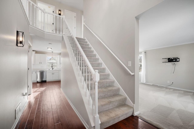 staircase featuring wood-type flooring, a high ceiling, ornamental molding, and sink