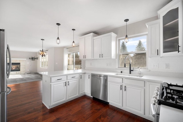 kitchen featuring sink, a stone fireplace, kitchen peninsula, white cabinets, and appliances with stainless steel finishes