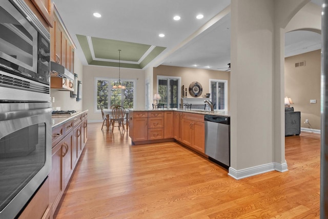 kitchen featuring ceiling fan with notable chandelier, a raised ceiling, hanging light fixtures, kitchen peninsula, and stainless steel appliances