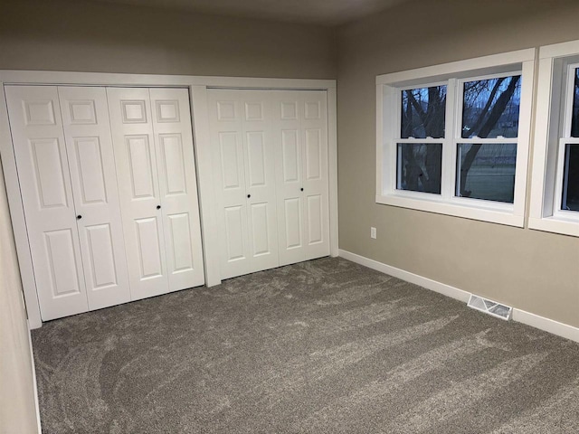 unfurnished bedroom featuring multiple closets and dark carpet