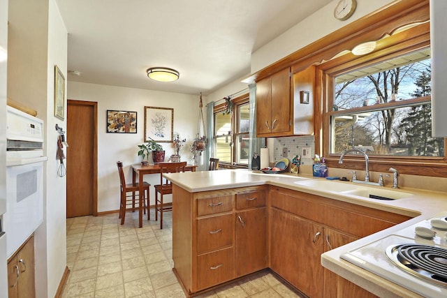 kitchen featuring plenty of natural light, kitchen peninsula, sink, and white appliances