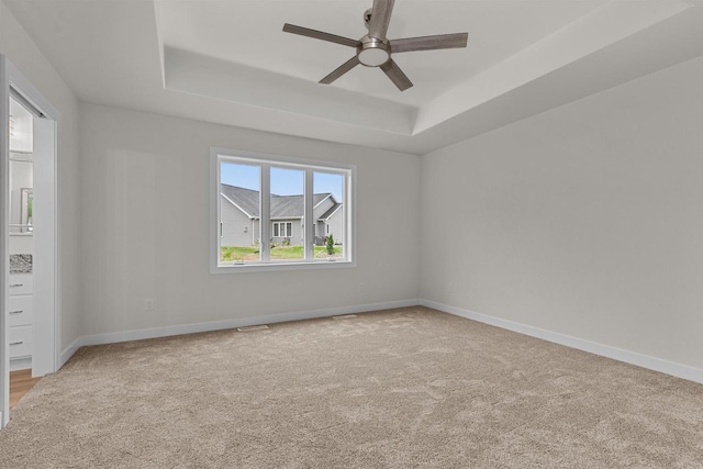 empty room with a tray ceiling, ceiling fan, and carpet floors