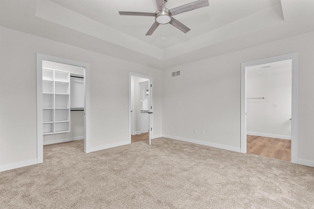 unfurnished bedroom with light carpet, a raised ceiling, ceiling fan, a spacious closet, and a closet