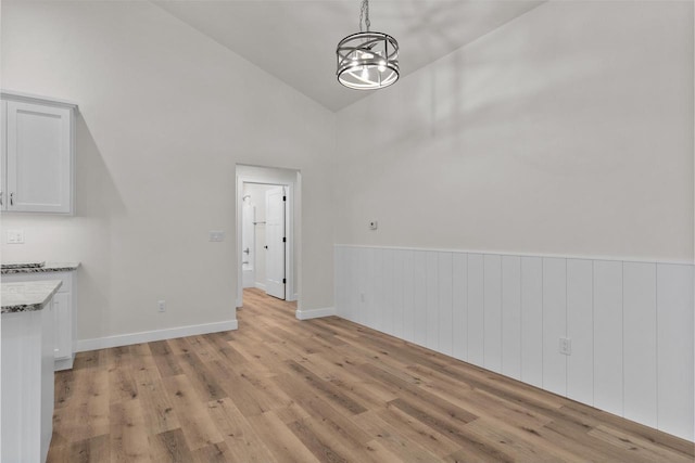 unfurnished dining area with light hardwood / wood-style floors, high vaulted ceiling, and a chandelier