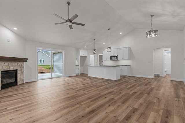 unfurnished living room featuring ceiling fan, sink, high vaulted ceiling, light hardwood / wood-style flooring, and a fireplace