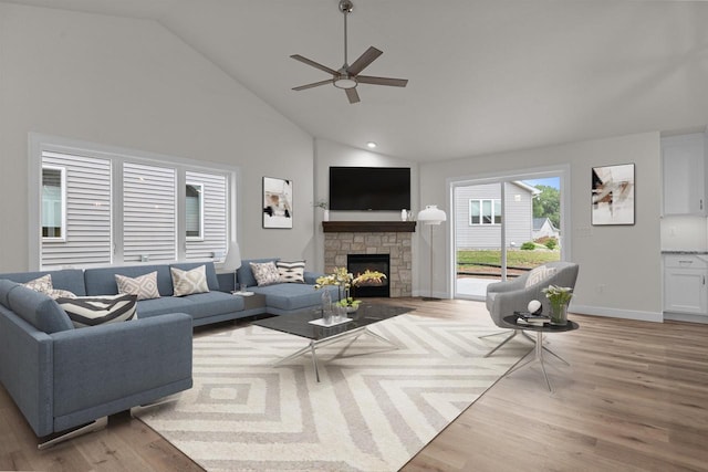 living room featuring a stone fireplace, ceiling fan, light hardwood / wood-style flooring, and high vaulted ceiling