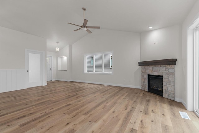 unfurnished living room with light wood-type flooring, a stone fireplace, ceiling fan, and lofted ceiling