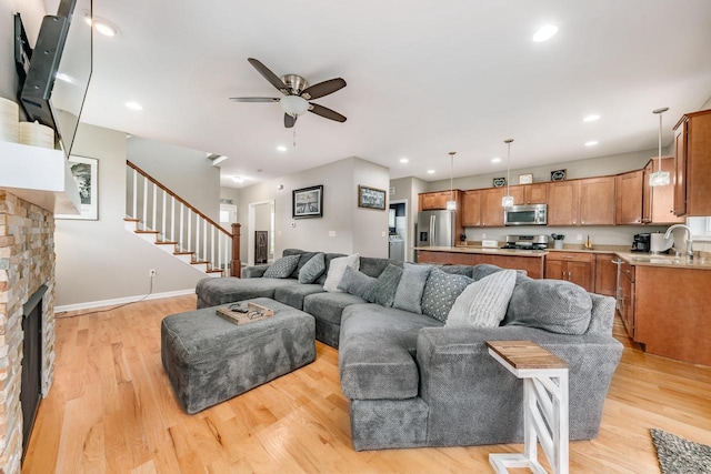 living room with a stone fireplace, ceiling fan, sink, and light hardwood / wood-style floors