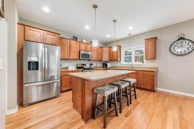 kitchen with a kitchen breakfast bar, hanging light fixtures, light hardwood / wood-style floors, appliances with stainless steel finishes, and a kitchen island