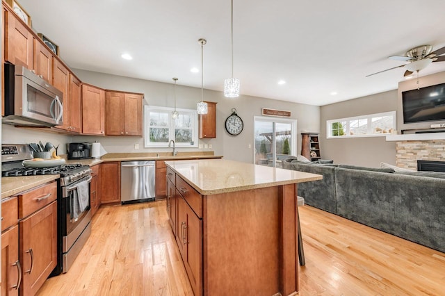 kitchen featuring light wood-type flooring, light stone counters, stainless steel appliances, ceiling fan, and a fireplace