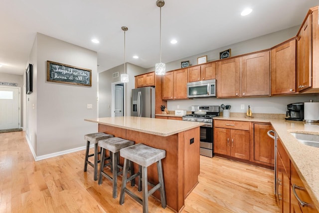 kitchen with stainless steel appliances, decorative light fixtures, a center island, light hardwood / wood-style floors, and a breakfast bar area