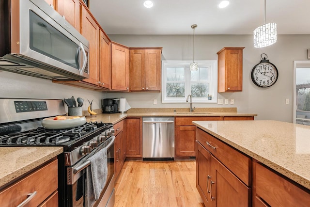 kitchen with light stone countertops, appliances with stainless steel finishes, light wood-type flooring, sink, and pendant lighting