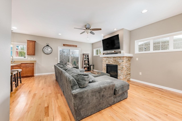 living room featuring ceiling fan, a fireplace, plenty of natural light, and light wood-type flooring