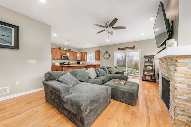 living room featuring ceiling fan, a stone fireplace, light wood-type flooring, and sink