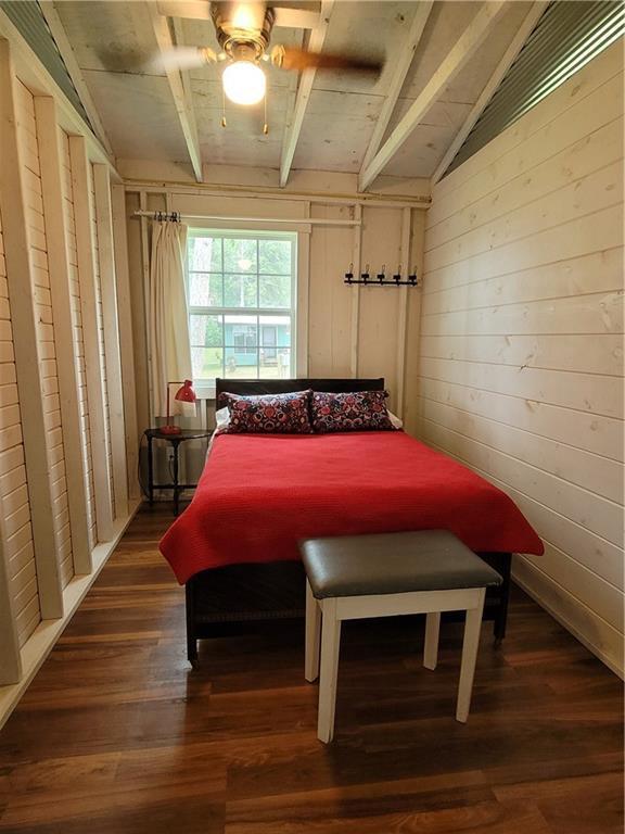 bedroom with lofted ceiling with beams, ceiling fan, dark wood-type flooring, and wood walls