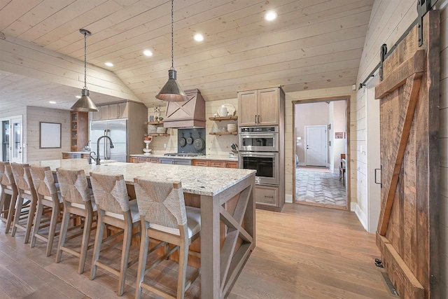 kitchen with stainless steel appliances, a barn door, light stone counters, pendant lighting, and custom exhaust hood