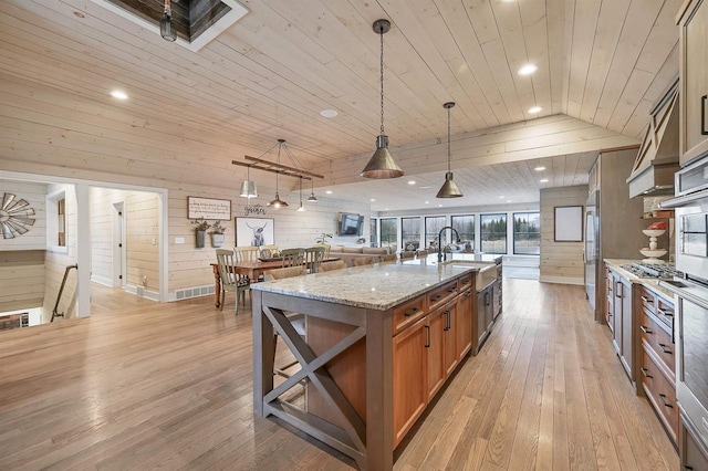 kitchen with pendant lighting, wood walls, wooden ceiling, a large island with sink, and light stone countertops