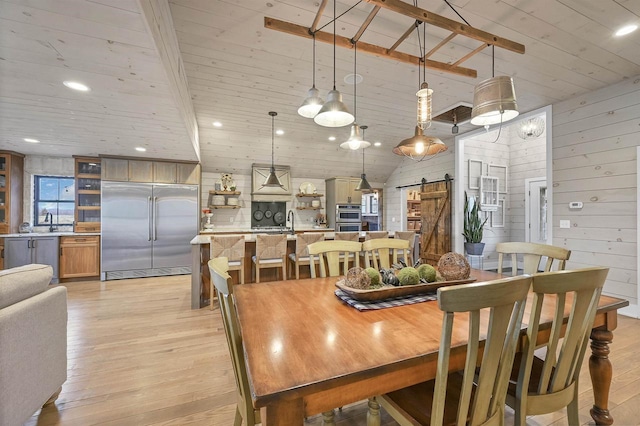 dining space featuring sink, wooden ceiling, a barn door, wooden walls, and light wood-type flooring