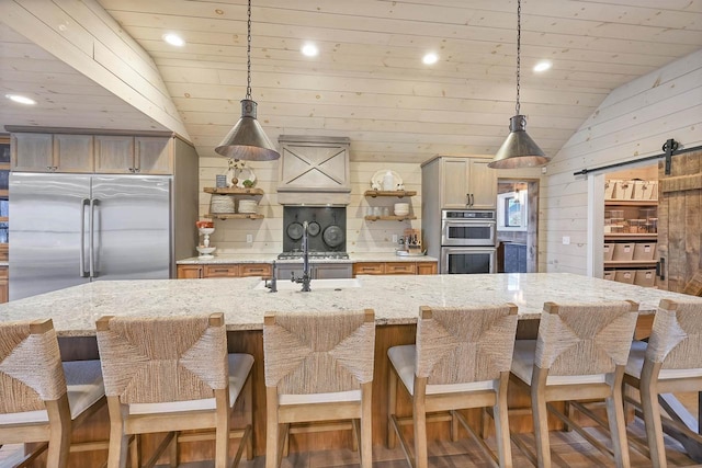 kitchen with a barn door, vaulted ceiling, a breakfast bar area, wooden walls, and appliances with stainless steel finishes