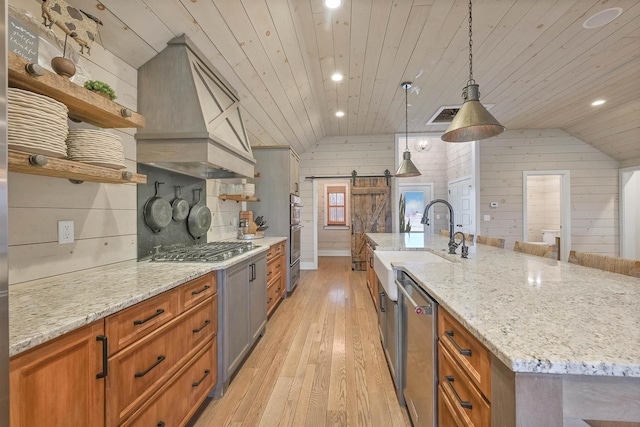 kitchen with stainless steel appliances, hanging light fixtures, wooden ceiling, a barn door, and wooden walls