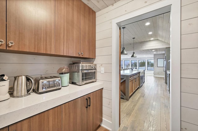 kitchen with sink, wooden ceiling, wood walls, pendant lighting, and light wood-type flooring