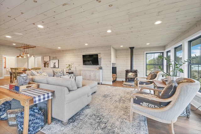 living room featuring wooden ceiling, wood walls, a wood stove, and light hardwood / wood-style flooring