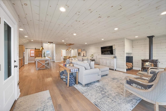 living room with light hardwood / wood-style floors, wood walls, wooden ceiling, and a wood stove