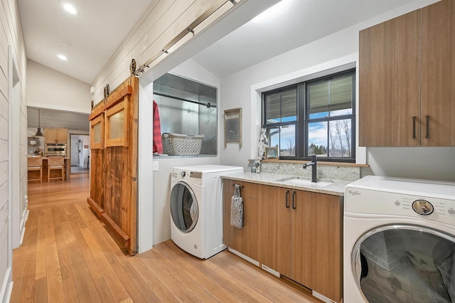 laundry room featuring sink, cabinets, a barn door, separate washer and dryer, and light hardwood / wood-style floors