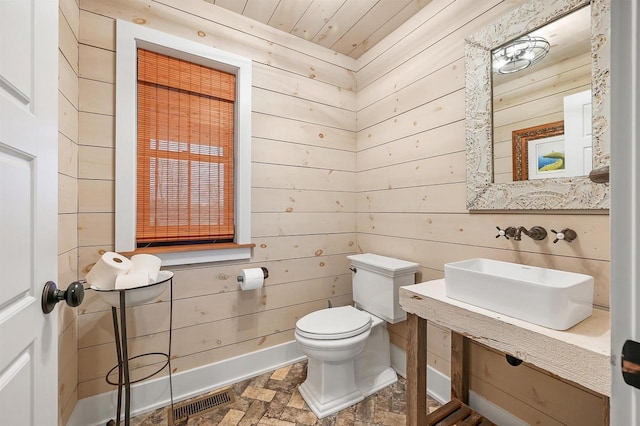 bathroom featuring sink, toilet, wood ceiling, and wood walls