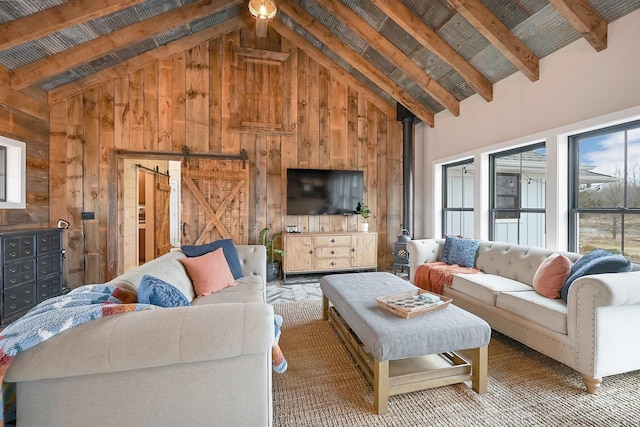 carpeted living room with beamed ceiling, a barn door, high vaulted ceiling, and wooden walls