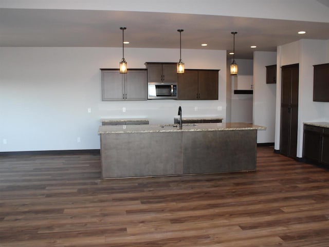 W4241 Hilltop Dr, Fond Du Lac, WI 54937 - kitchen featuring dark wood-type flooring, hanging light fixtures, light stone counters, a kitchen island with sink, and dark brown cabinets