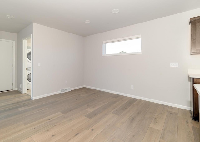 unfurnished living room with visible vents, light wood-style flooring, stacked washing maching and dryer, and baseboards