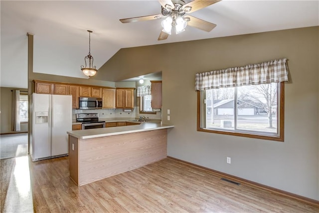 kitchen with pendant lighting, vaulted ceiling, light wood-type flooring, kitchen peninsula, and stainless steel appliances