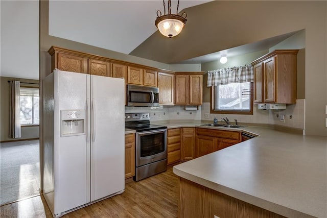 kitchen with sink, vaulted ceiling, decorative light fixtures, light hardwood / wood-style floors, and stainless steel appliances