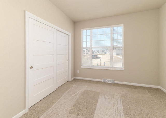 unfurnished bedroom featuring carpet, visible vents, baseboards, and a closet