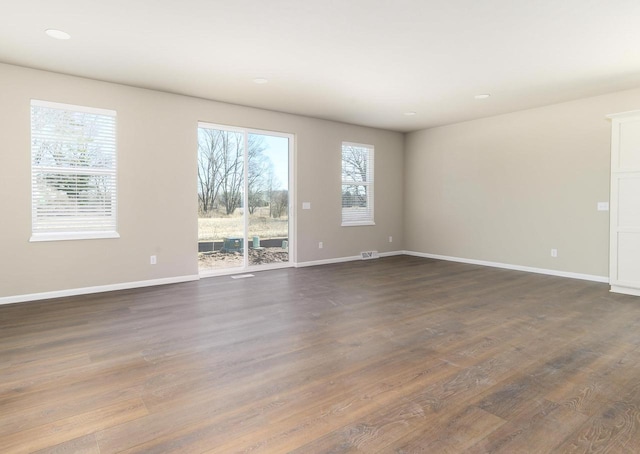 unfurnished room featuring dark wood-style flooring, baseboards, and a wealth of natural light