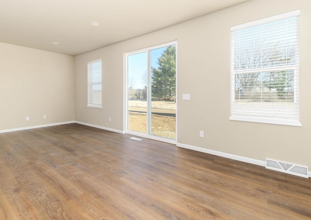 empty room with dark wood-style floors, visible vents, and baseboards