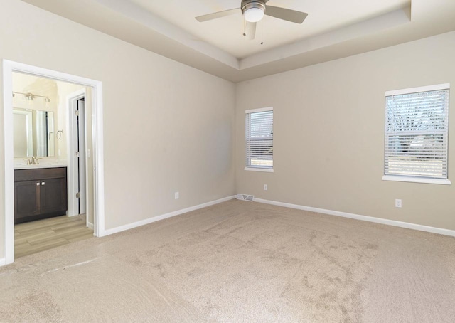 empty room with a ceiling fan, baseboards, visible vents, a tray ceiling, and light carpet