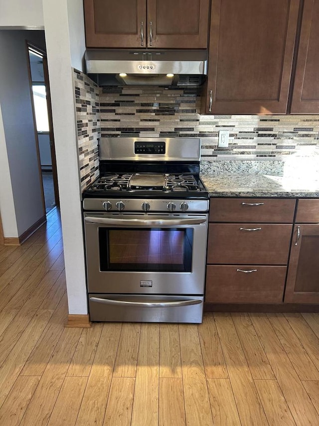 kitchen featuring decorative backsplash, dark brown cabinetry, light stone countertops, and stainless steel gas range oven