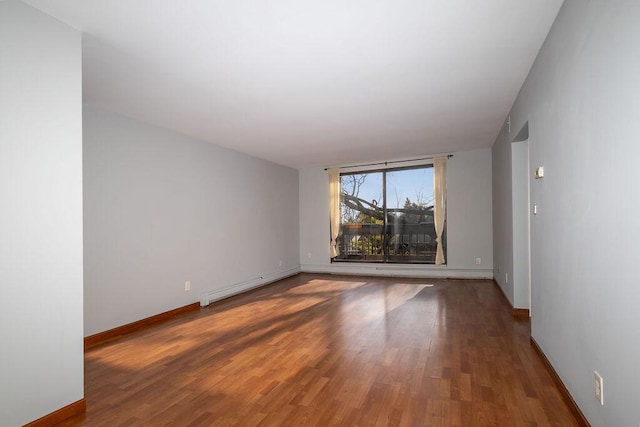 spare room featuring a baseboard radiator, wood finished floors, and baseboards