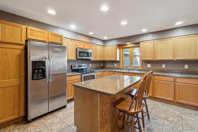 kitchen featuring a kitchen breakfast bar, stainless steel appliances, sink, dark stone countertops, and a center island