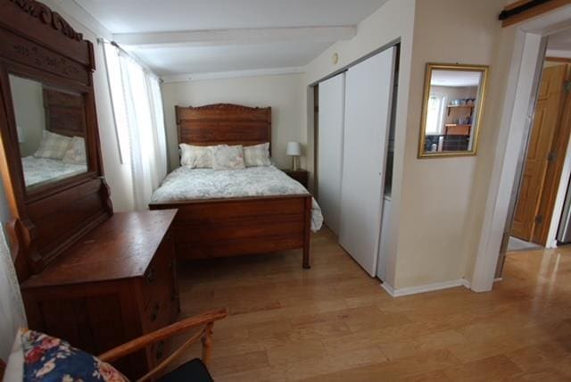 bedroom with a closet, beamed ceiling, and light hardwood / wood-style flooring