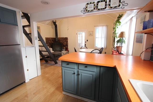 kitchen with stainless steel refrigerator, a wood stove, sink, blue cabinets, and light wood-type flooring