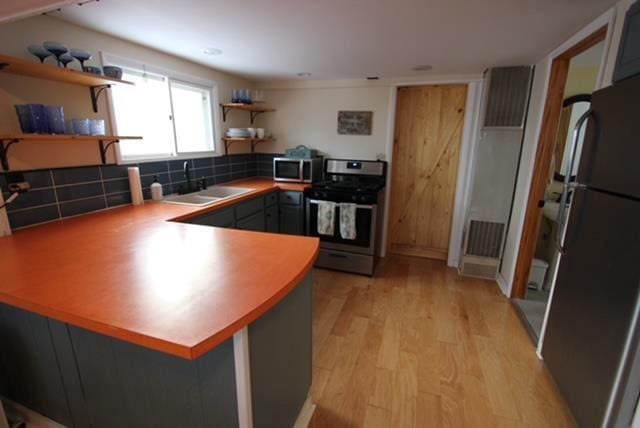 kitchen with light hardwood / wood-style floors, kitchen peninsula, sink, and appliances with stainless steel finishes