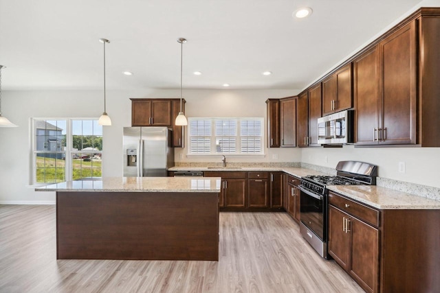 kitchen featuring decorative light fixtures, appliances with stainless steel finishes, a kitchen island, light stone countertops, and light hardwood / wood-style floors