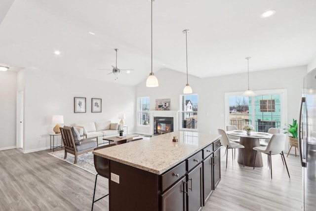 kitchen featuring a healthy amount of sunlight, decorative light fixtures, light stone countertops, and dark brown cabinets