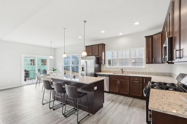 kitchen featuring sink, appliances with stainless steel finishes, hanging light fixtures, light stone countertops, and a kitchen island